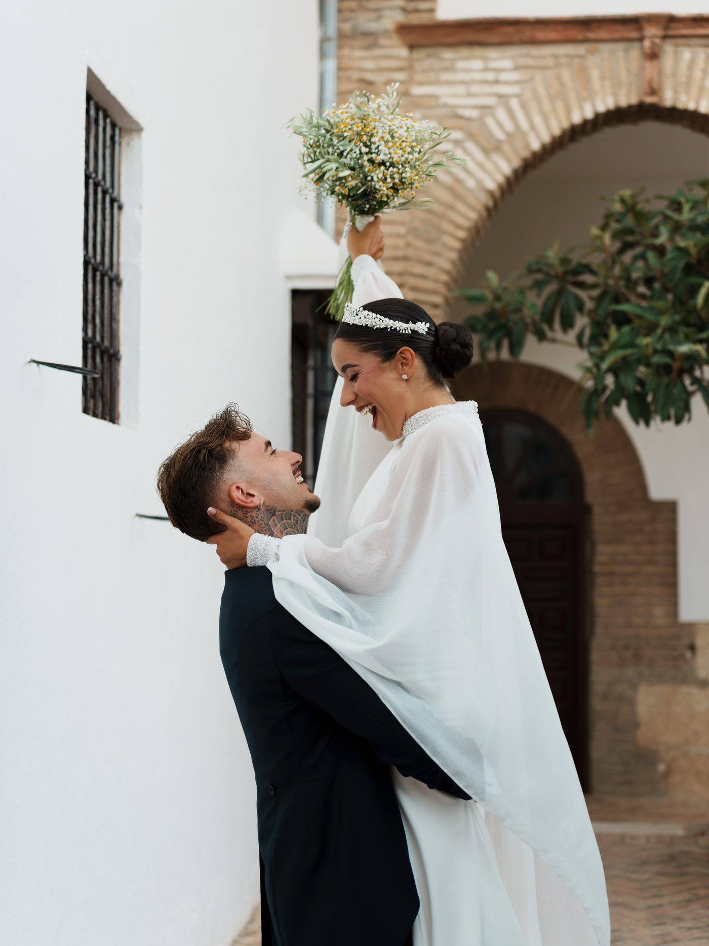 El novio levanta a la novia, que alza el ramo riéndose