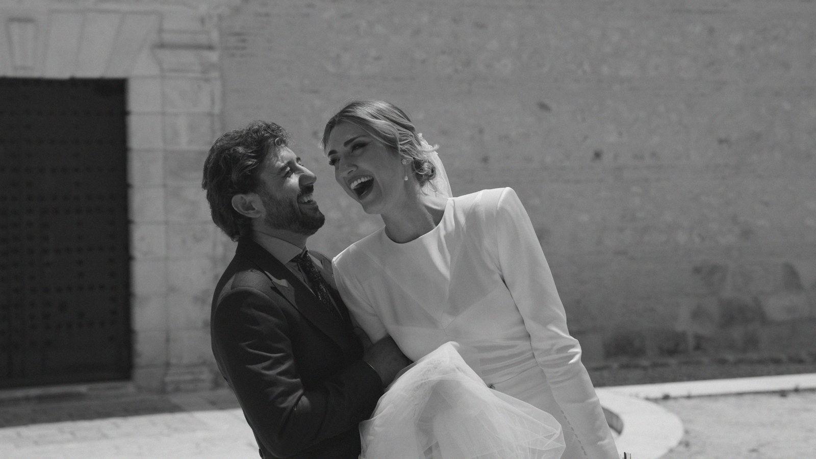 Los novios riéndose sentados junto al muro