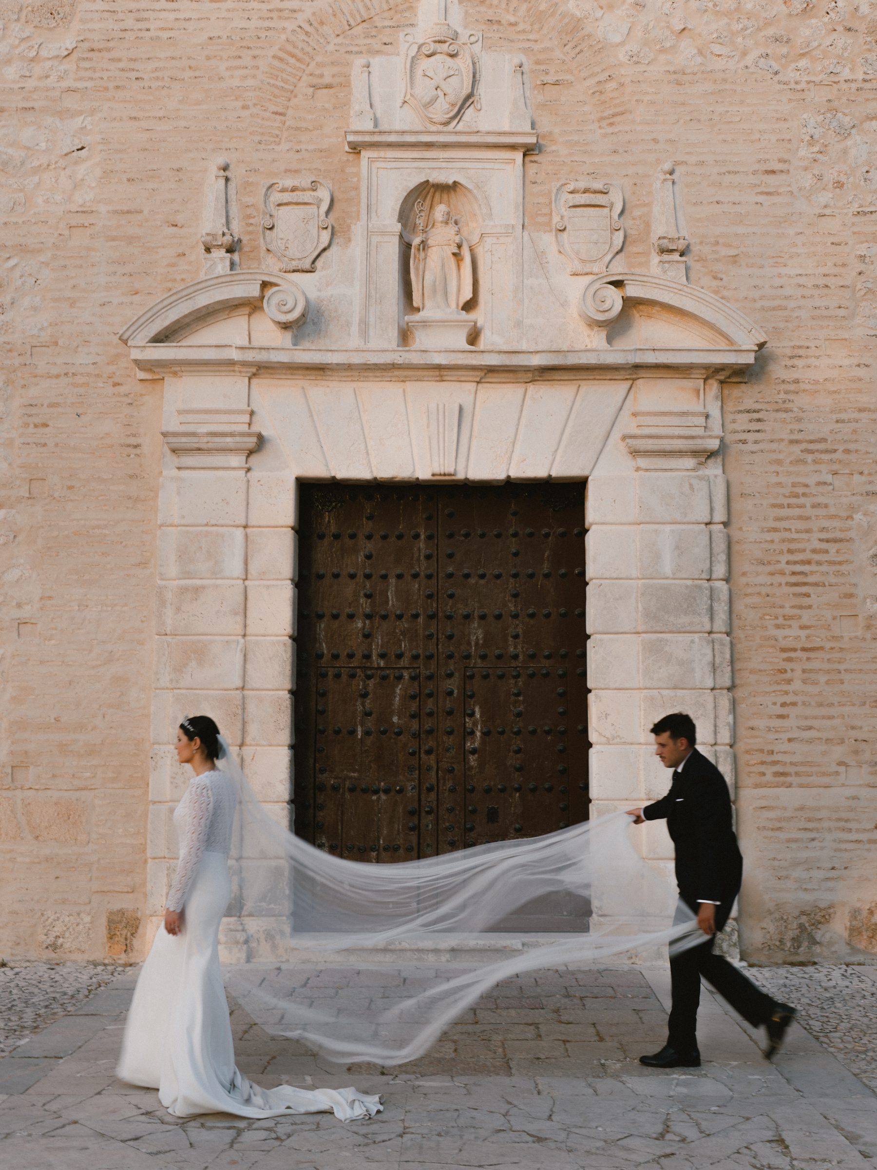 Los novios sosteniendo el velo frente a la portada de la iglesia